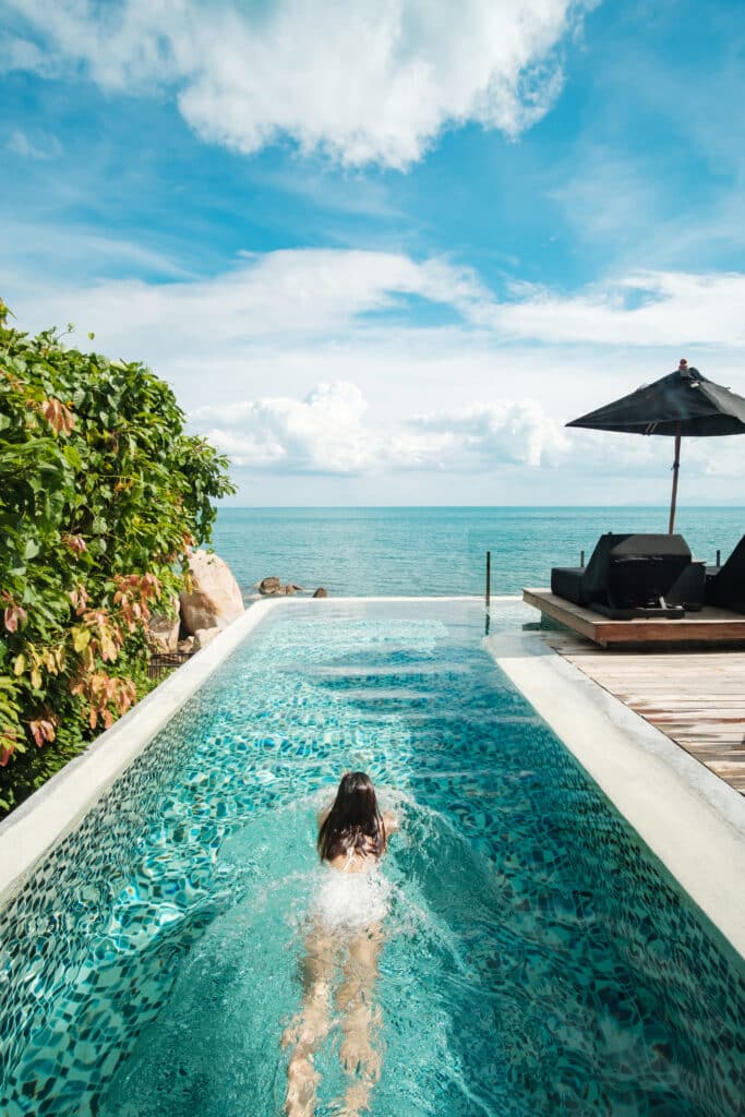 Femme nageant dans une piscine à débordement avec vue sur l'océan turquoise sous un ciel bleu. Ambiance tropicale de luxe.