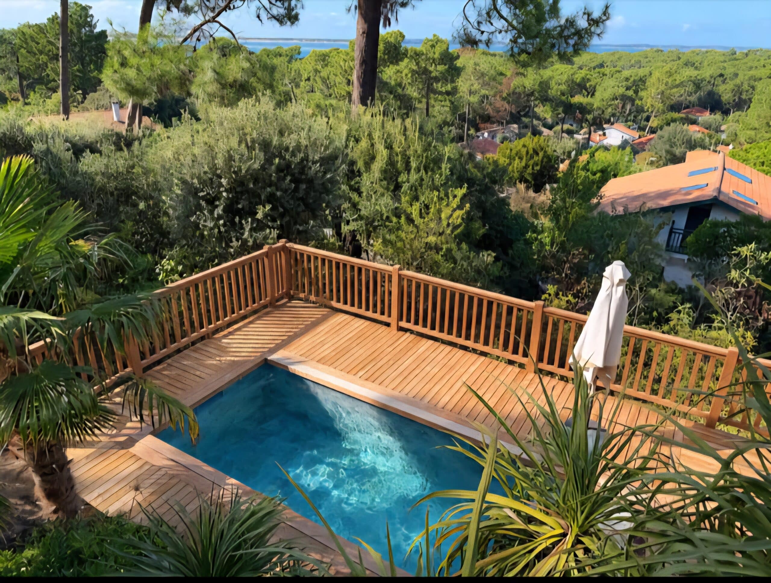 Petite piscine sur terrasse en bois entourée de palmiers et forêt avec vue lointaine sur la mer.